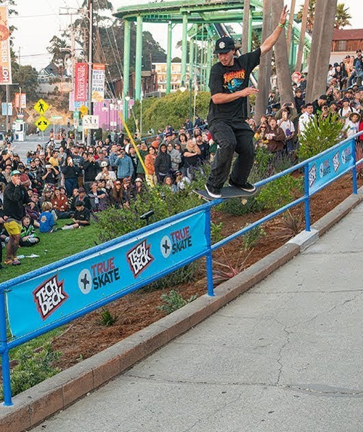 Santa Cruz Skateboards 50th anniversary celebration. A skateboarder grinds a rail surrounded by a crowd of people.