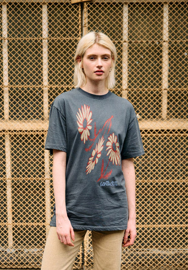 Woman wearing a slate Santa Cruz Dizzy Daisy t-shirt with floral design in front of a textured wall.