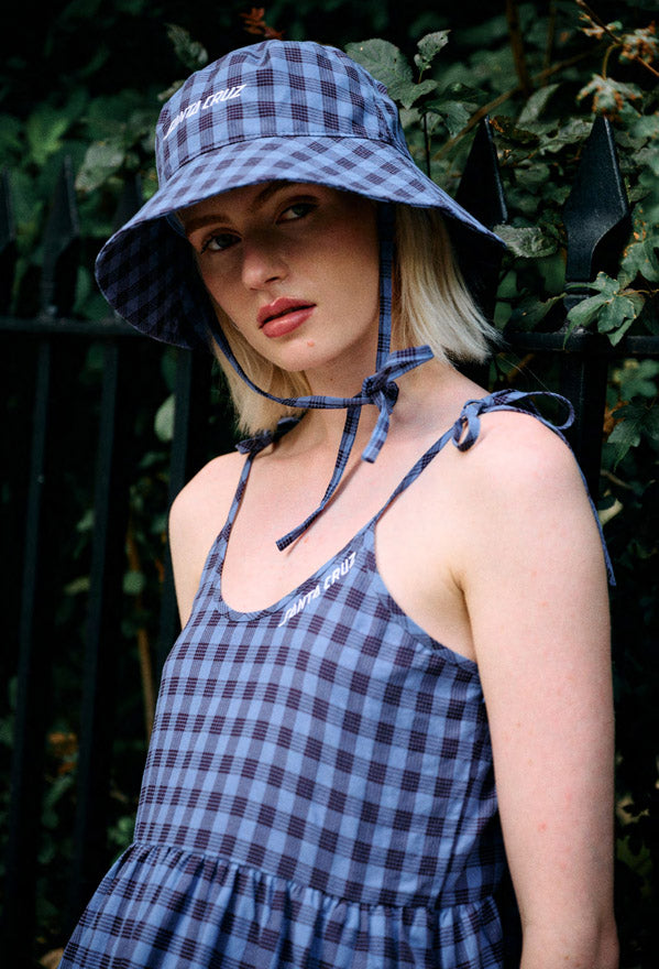 Woman wearing a lavender checked Santa Cruz Strip Midi dress and bucket hat against a green leafy background