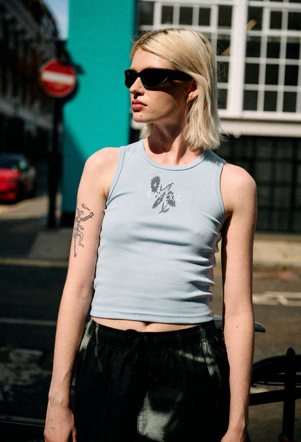 Woman wearing a light blue Santa Cruz Dizzy Daisy Strip tank top with a flower graphic design outdoors.