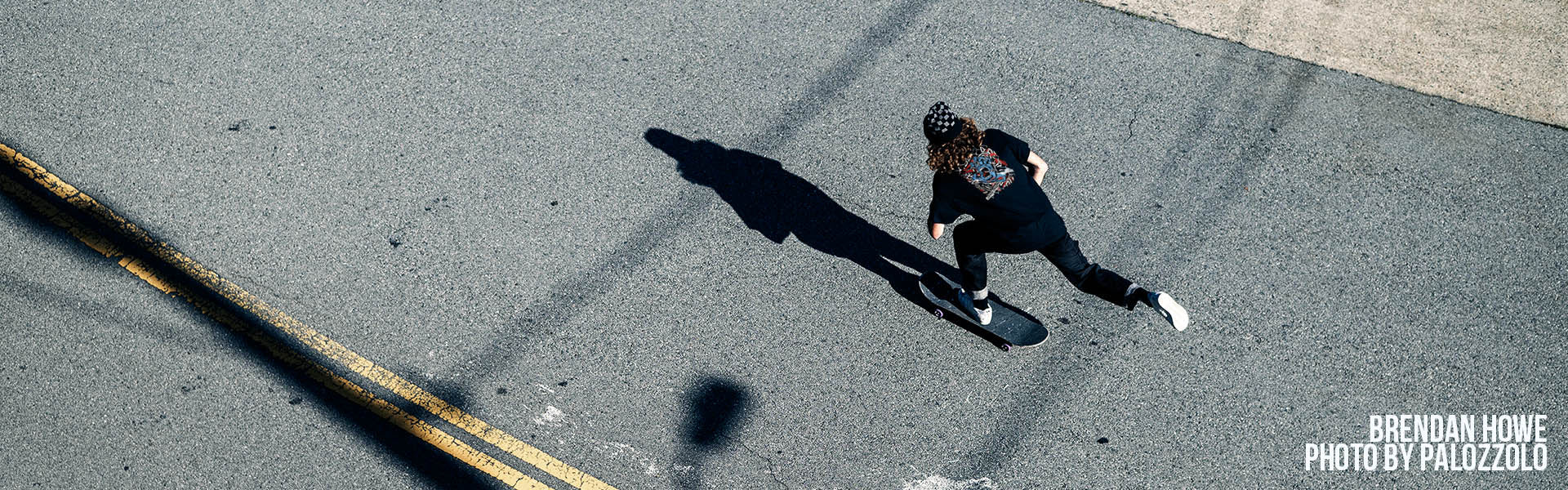 A high-angle photograph of Brendan Howe skating on a Santa Cruz skateboard, casting a long shadow.