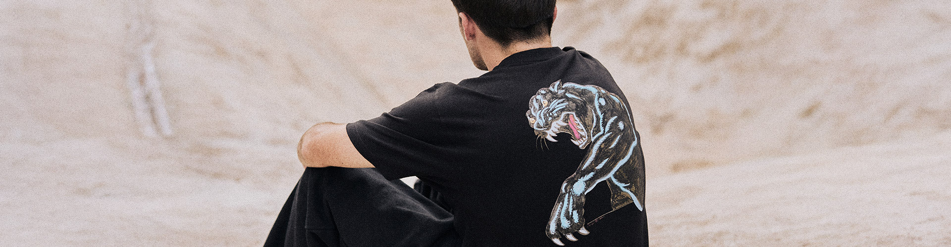 Santa Cruz Natas Sketch Panther Graphic Collection. A man with short dark hair, seen from behind, wears a black Santa Cruz t-shirt featuring a dynamic, roaring panther graphic.