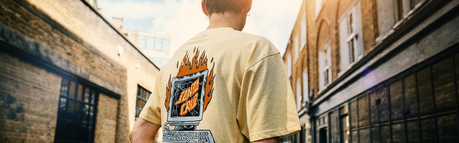 Person wearing a custard Santa Cruz t-shirt with Self Destruct graphic design in an urban setting