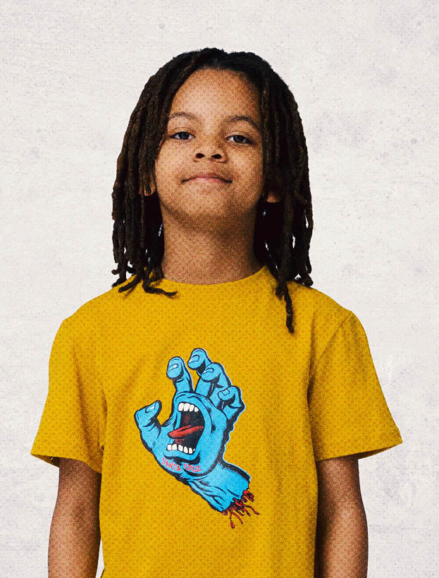 Child wearing a yellow Santa Cruz t-shirt with a blue screaming hand graphic design on a light gray background